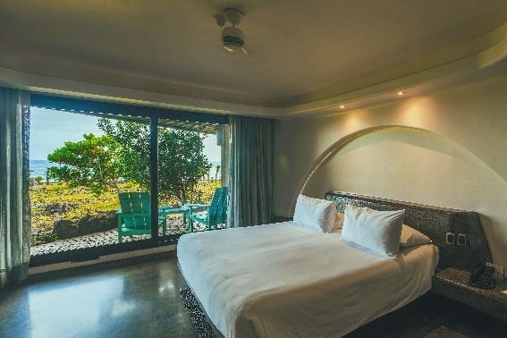 Habitación Kainga con cama king y ventanal hacia la terraza y el océano.