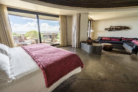 Suite Maunga con cama king, sala de estar y ventanal con vista al mar.